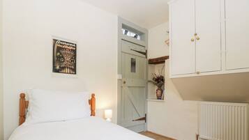 A bedroom with a bed, a nightstand, a wall-mounted lamp, a door leading to another room, and a radiator.