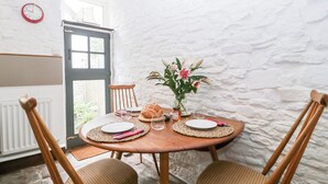 En spiseplads med et rundt bord dækket til to personer, en vase med blomster og et ur på væggen.
