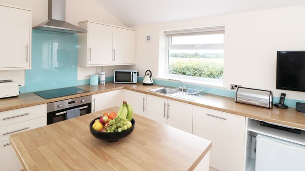 A modern kitchen with white cabinets, a microwave, a kettle, and a bowl of fruit on the counter. - Bowler Yard Cottage (Mansfield)