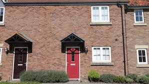 Un bâtiment en briques avec une porte rouge, des fenêtres blanches et un toit recouvert de tuiles.