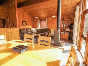Ein Holzinterieur mit einer Couch, einem Esstisch, Stühlen, einem Bücherregal und einem Kamin.