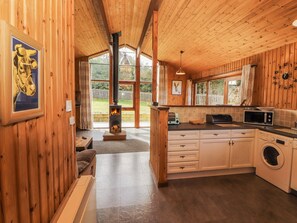 Ein Interieur einer Holzhütte mit Küche, Kamin und großem Fenster.