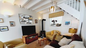 A living room with a sofa, armchair, and a TV stand with books. - Crab Cottage (Ilfracombe)