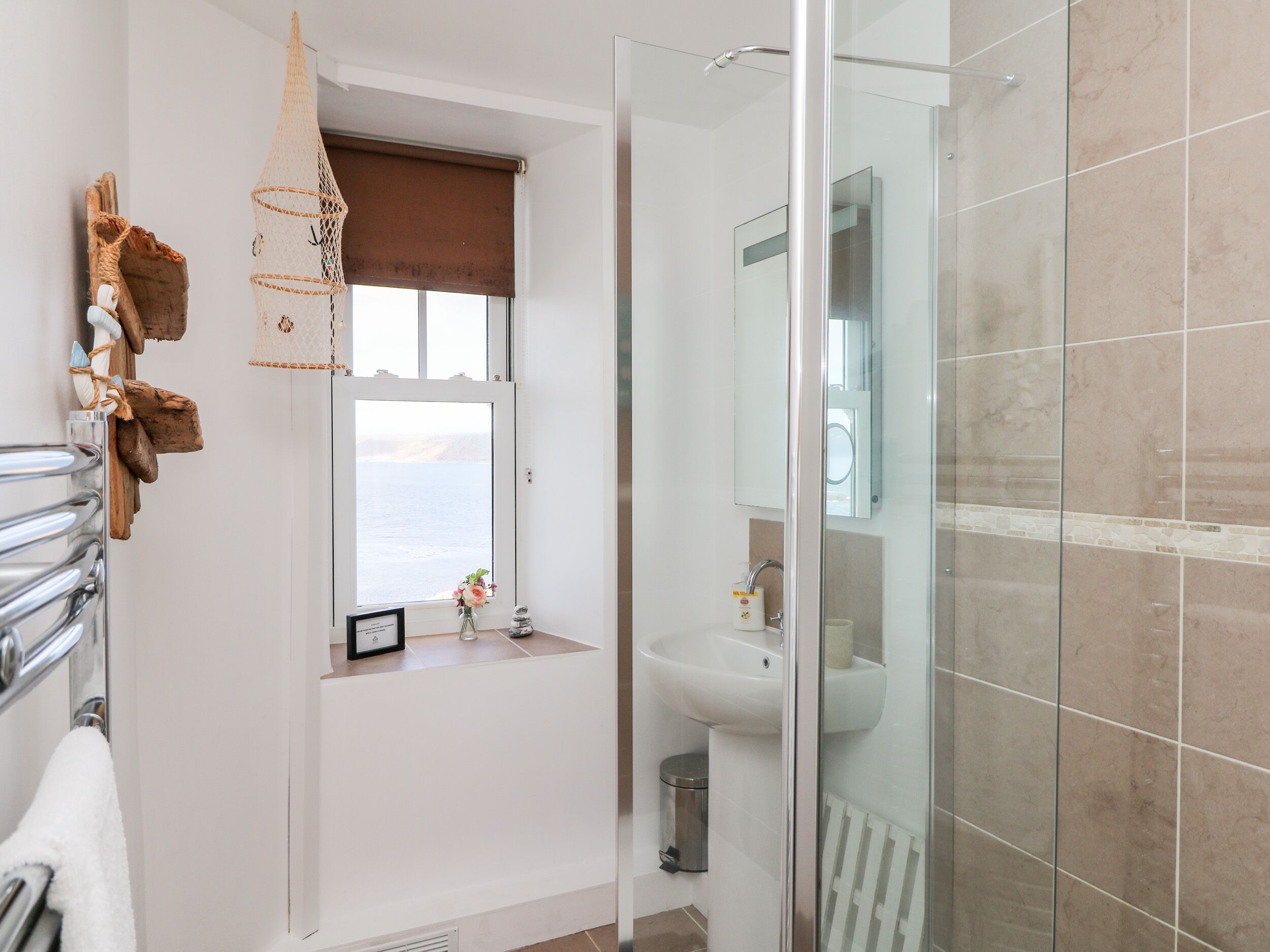 A bathroom with a glass shower enclosure, a sink, a window with a view, and a towel rack.