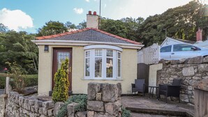 A small house with a stone wall, a red-tiled roof, and a bay window. - Llidiart Cerrig (Rhyl)