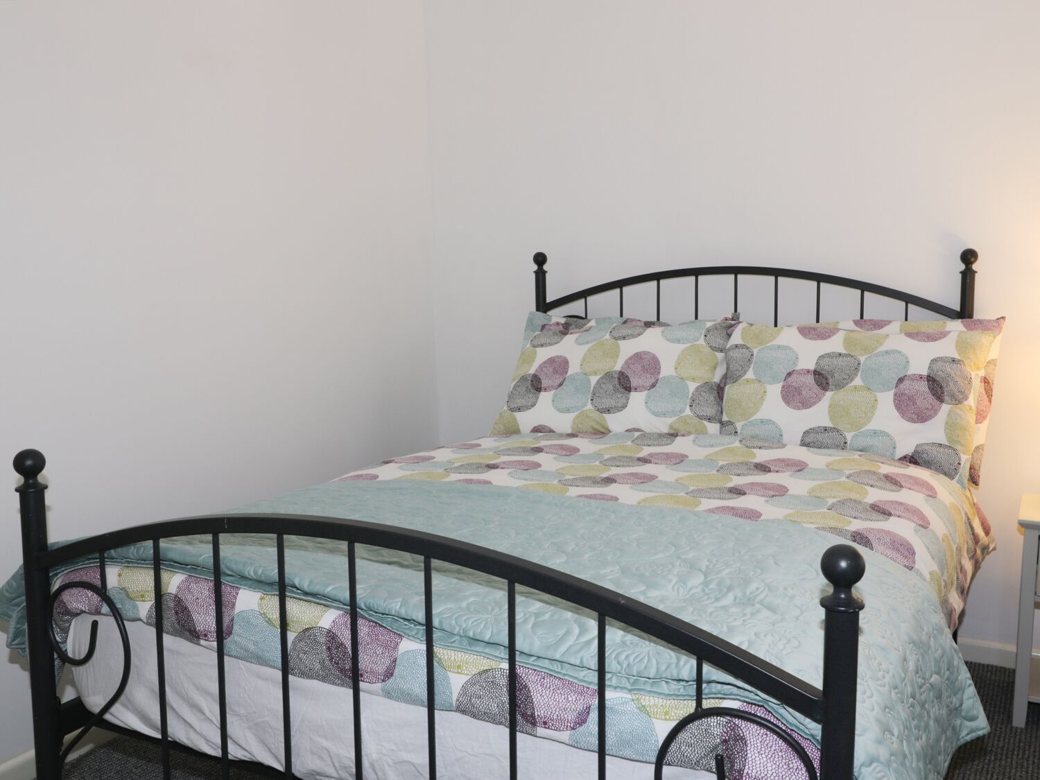A bed with a black metal frame, a quilt with a polka dot pattern, and a white pillow.