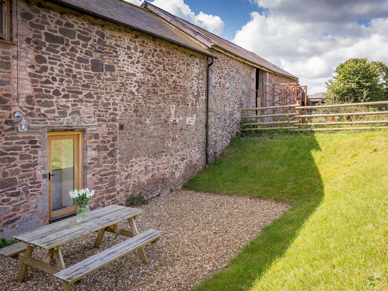 A stone building with a wooden door and a picnic table with a vase of flowers.