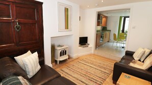 A living room with a dark brown leather sofa, a wooden cabinet, and a television on a small white stand. There is a striped rug on the floor and a wooden coffee table with a remote control on it. - Mill Bridge Cottage (Hope Valley)