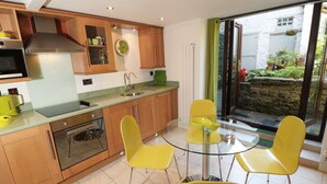 A modern kitchen with wooden cabinets, a stainless steel range hood, and a glass dining table with yellow chairs. - Mill Bridge Cottage (Hope Valley)