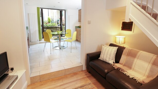 A modern living room with a brown leather sofa, a glass coffee table, and yellow chairs. - Mill Bridge Cottage (Hope Valley)