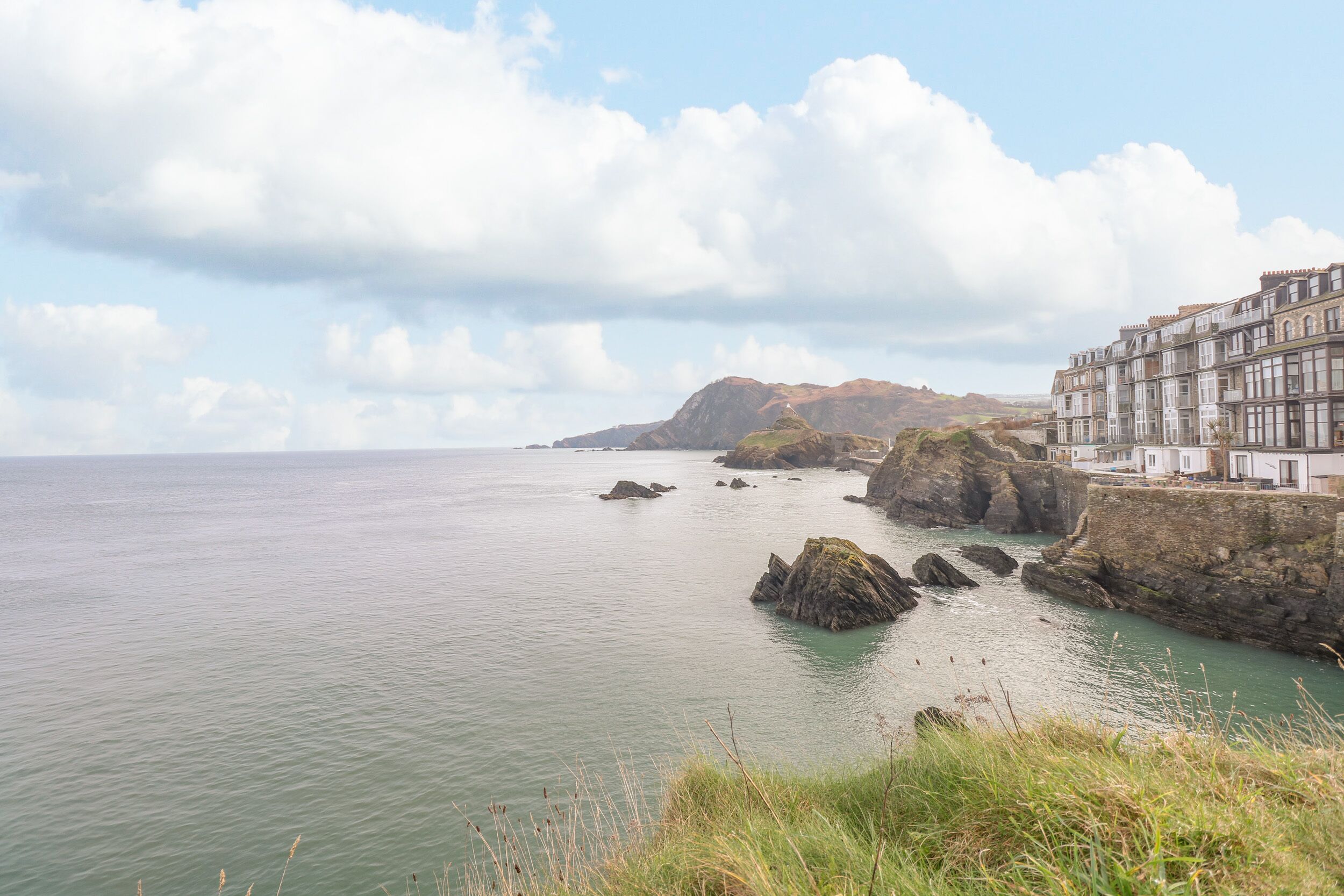 A coastal scene with a building adjacent to the sea, featuring a rocky shoreline and a clear sky.