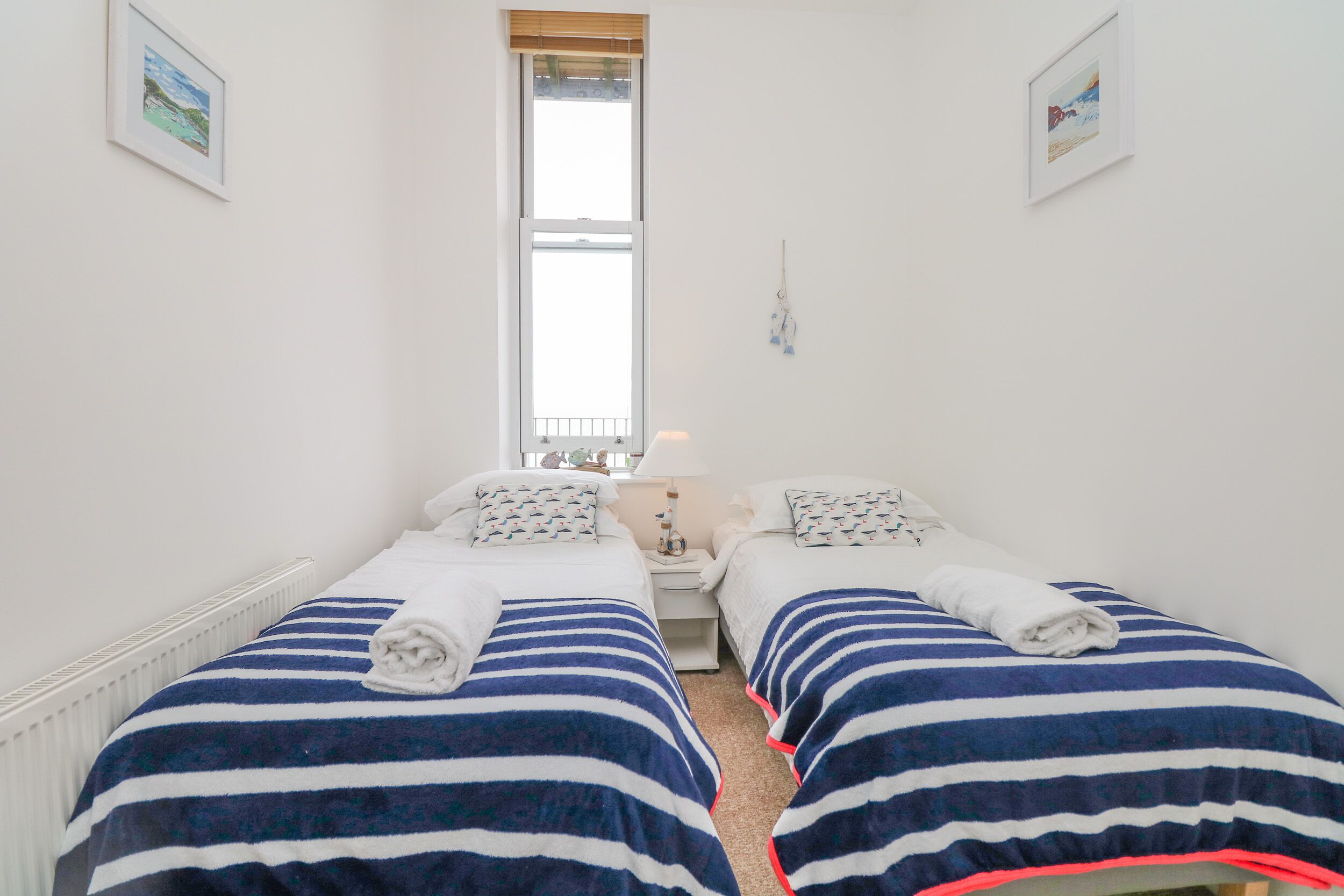Habitación doble con dos camas, cada una con ropa de cama y toallas a rayas, una ventana y una mesita de noche pequeña con lámpara.
