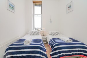 A twin room with two beds, each with striped bedding and towels, a window, and a small bedside table with a lamp.