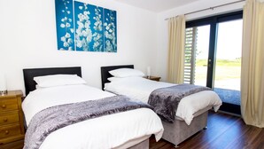 Een tweepersoonskamer met twee bedden, een groot raam met gordijnen, een houten vloer en een blauw bloemenkunstwerk aan de muur.