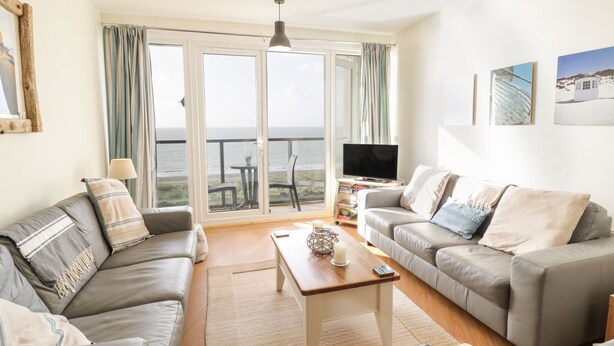 A living room with two sofas, a coffee table, a TV, and a balcony with a view of the sea. - 12 West End Point (Pwllheli)
