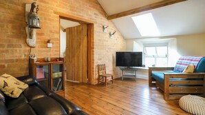 Un salón estilo loft con paredes de ladrillo visto, vigas de madera, un sofá de cuero, un televisor y un ventanal que deja entrar luz natural.
