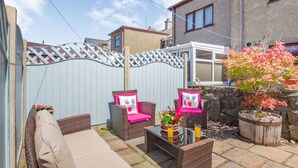 A patio with wicker furniture, a table with drinks, and a potted plant. - 40 New Row (Pwllheli)