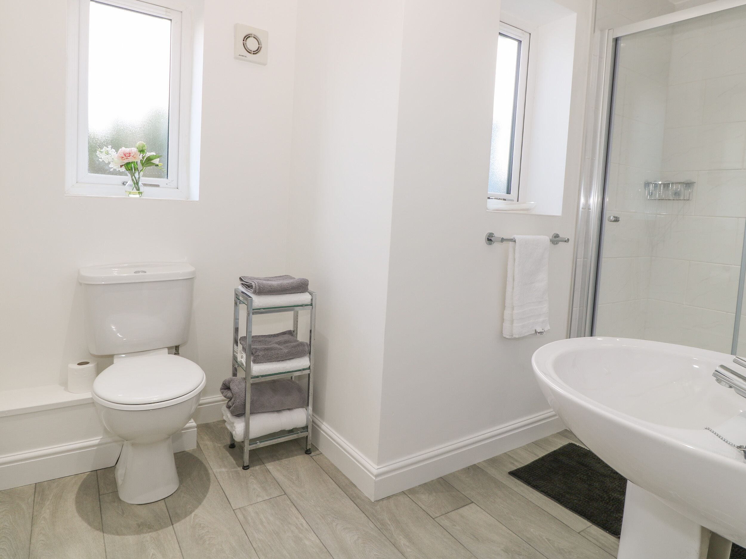 A bathroom with a toilet, a glass shelf with towels, a sink, and a shower area.