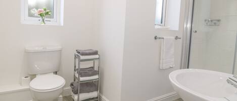 A bathroom with a toilet, a glass shelf with towels, a sink, and a shower area.