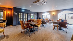 A spacious indoor area with multiple seating arrangements, including tables and chairs, and large windows providing natural light. - Dotty's Sunshine Cottage (Filey)