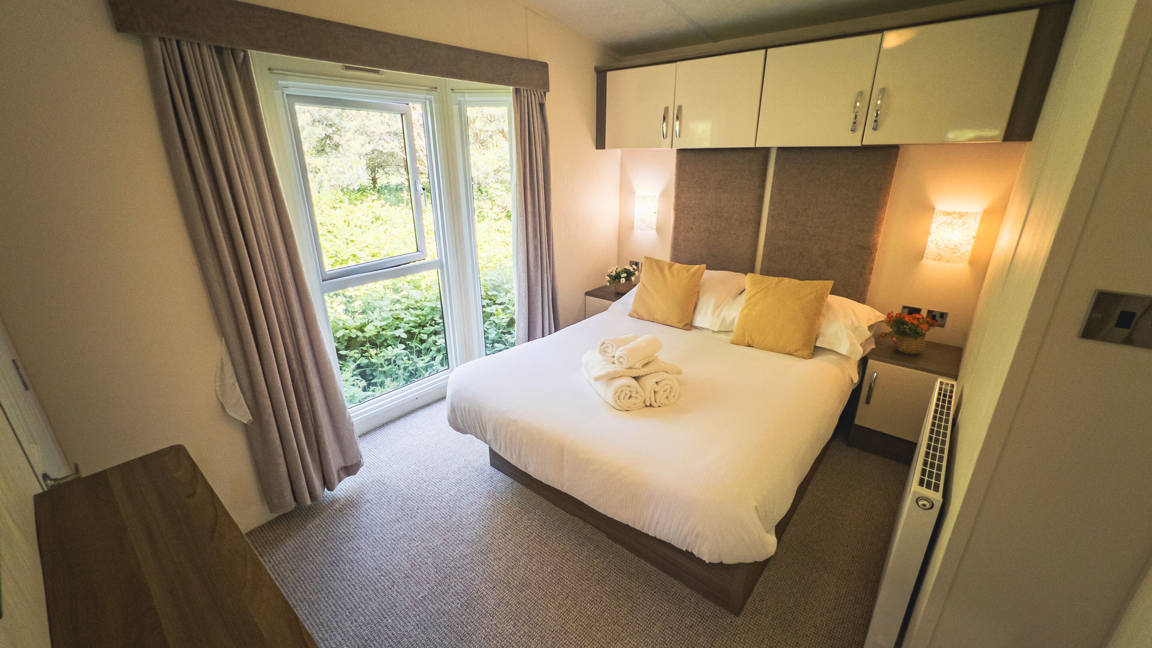 A neatly made bed with rolled towels, a nightstand with a lamp, and a window with curtains.
