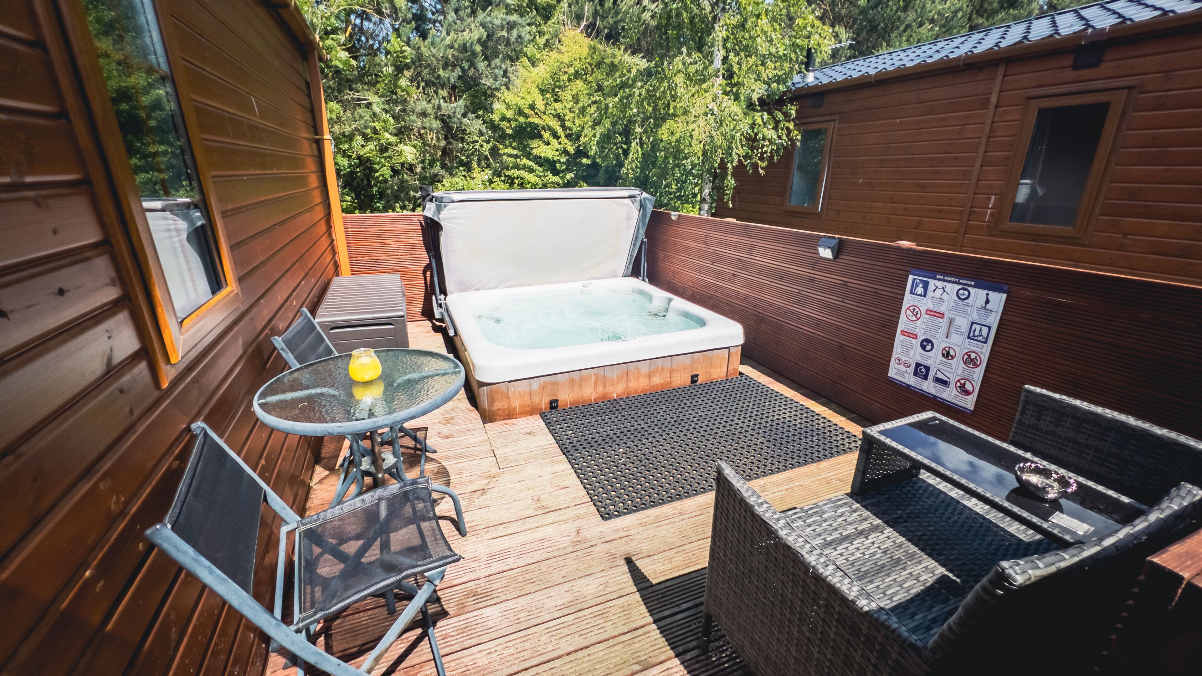 A wooden deck with a hot tub, a glass table with a yellow drink, and a safety sign.