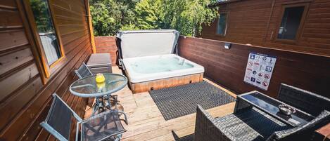 A wooden deck with a hot tub, a glass table with a yellow drink, and a safety sign.