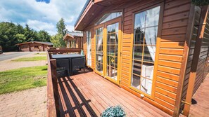 A wooden cabin with a deck, large windows, and a patio area. - Angie's Haven (Morpeth)