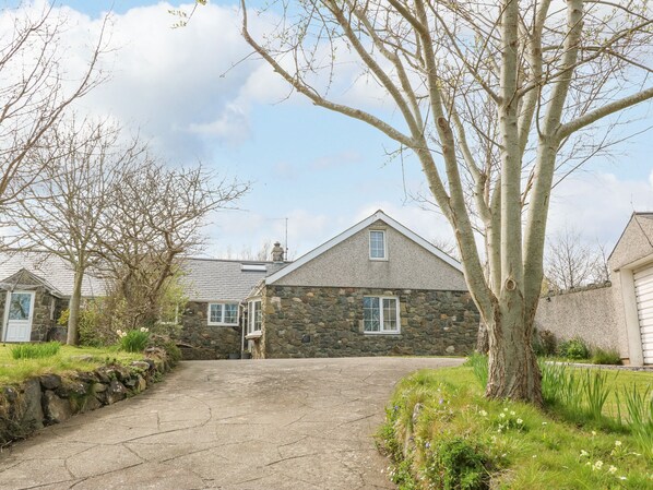 A stone house with a sloped roof, a stone wall, and a paved driveway.