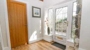 A wooden door, a framed picture, a stone wall, and a window with a view of greenery. - Glan Felin (Pwllheli)