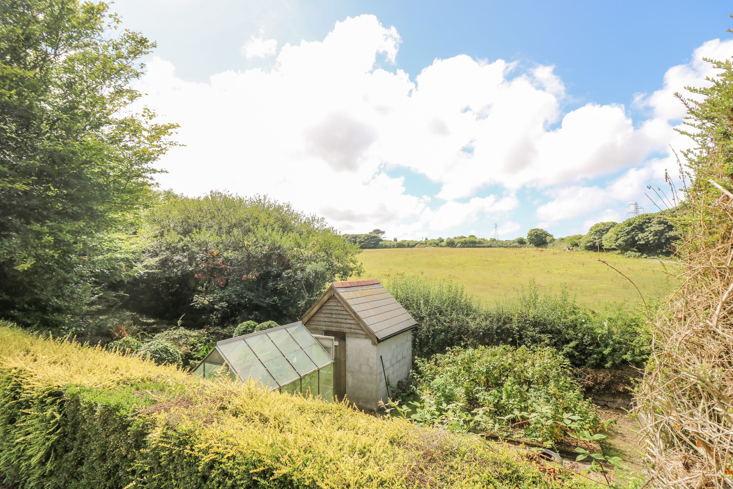 A small, rustic wooden shed in a lush, green landscape with a clear sky.