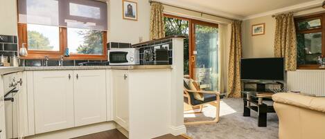 A modern kitchen with white cabinets, a microwave, and a sink. There is a dining area with a chair and a TV.