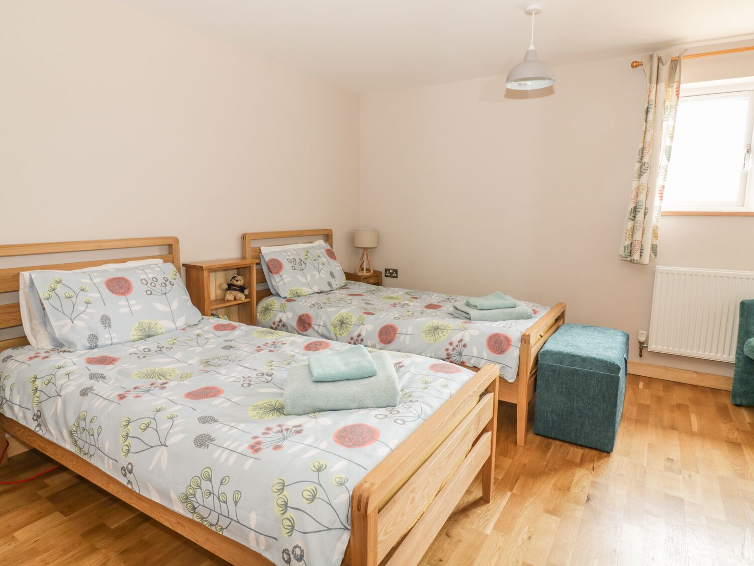 A bedroom with two wooden beds, a nightstand, a lamp, a window with curtains, and a radiator.