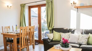 A cozy living room with a wooden dining table, chairs, a black leather sofa with patterned cushions, and a small wooden coffee table. - Clun Forest Cottage (Much Wenlock)
