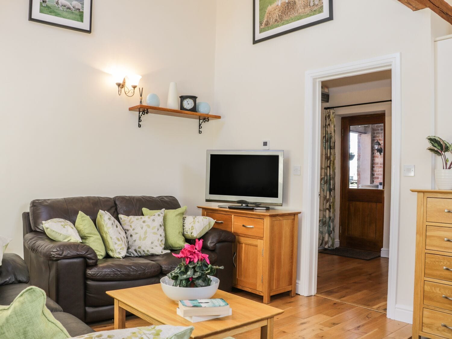 Una sala de estar con un sofá de cuero, una mesa de centro de madera con una planta, un televisor sobre un mueble de madera y un estante montado en la pared con objetos decorativos.