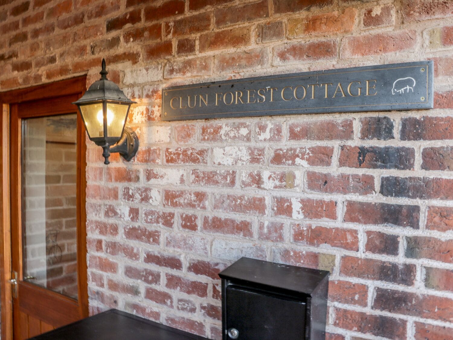 A brick wall with a sign reading "CLUN FOREST COTTAGE" and a black cabinet.