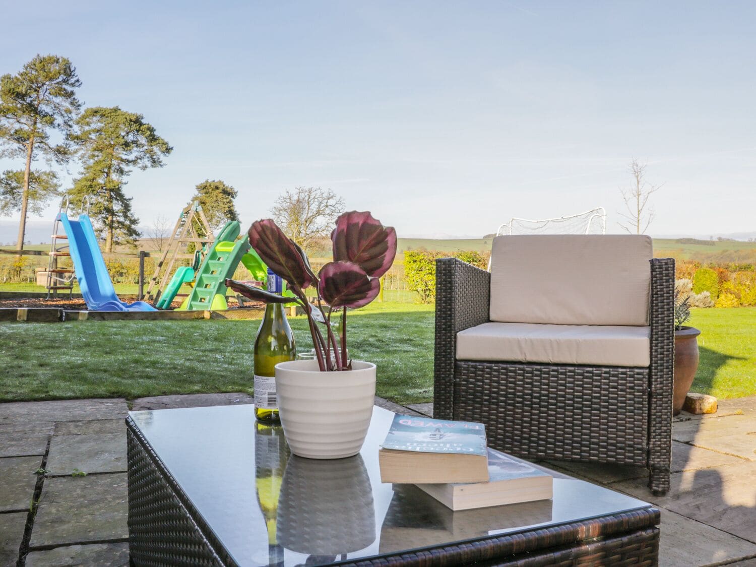 An outdoor seating area with a glass-top table, a wicker chair, and a book.