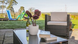An outdoor seating area with a glass-top table, a wicker chair, and a book. - Clun Forest Cottage (Much Wenlock)