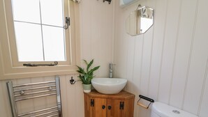 Un bany amb un vàter blanc, un moble de fusta amb un lavabo, una barra de tovalloles i una planta en test.
