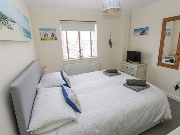 A bedroom with a bed, a television, a window, and artwork on the walls. - Sandy Bay House (Saundersfoot)
