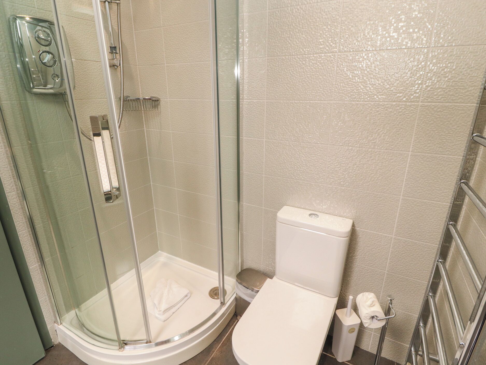 Een badkamer met een douche met glazen wand, een toilet en een handdoekhouder.
