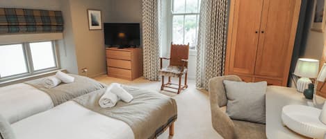 Habitación de hotel con dos camas, televisión, armario de madera, una silla y un escritorio con lámpara.