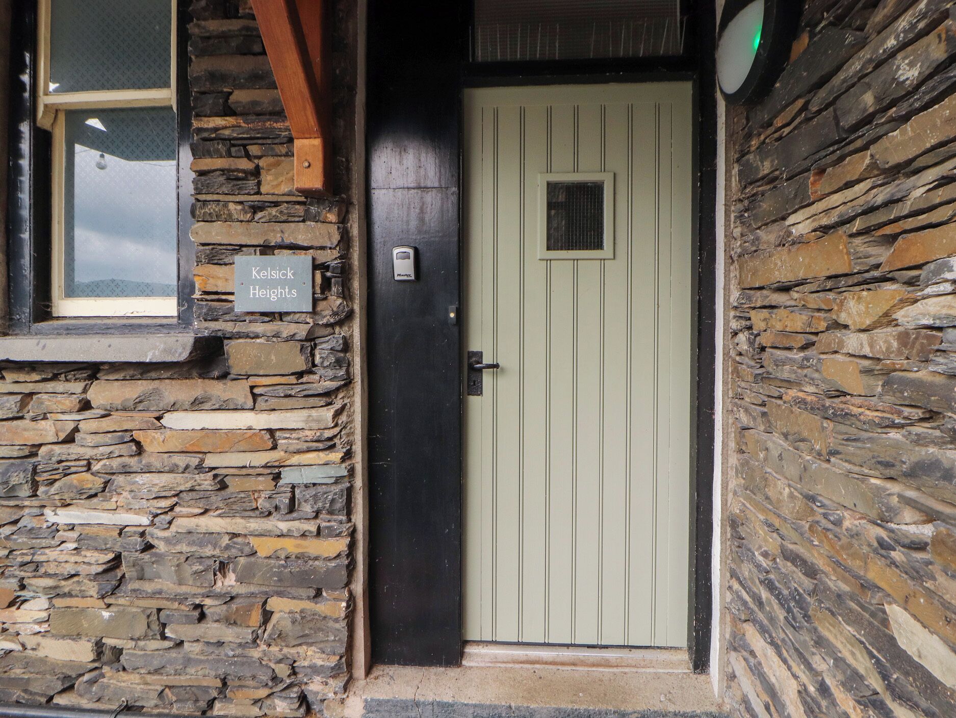 A stone building with a green door, a sign reading 'Kelsick Heights,' and a window with a view.
