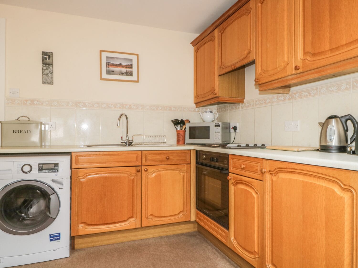 A kitchen with wooden cabinets, a washing machine, a microwave, and a kettle.