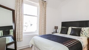Un dormitorio con cama, mesita de noche, lámpara y ventana con cortinas.