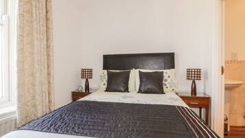 A bedroom with a bed, two bedside tables, a headboard, and a window with curtains.