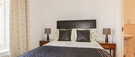 Un dormitorio con cama, dos mesitas de noche, cabecero y ventana con cortinas.