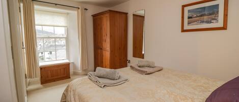 Ein Schlafzimmer mit einem großen Bett, einem Holzschrank, einem Fenster mit Vorhängen und einem gerahmten Bild an der Wand.