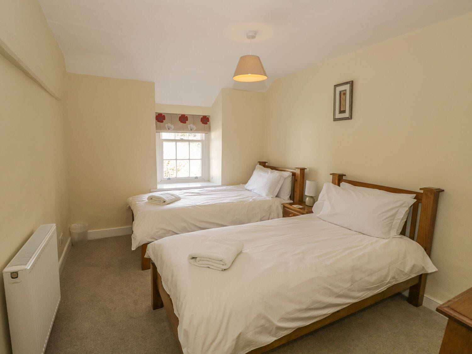 A bedroom with two single beds, a window with a view, a radiator, and a bedside table with a lamp.