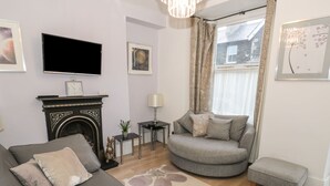 A living room with a grey sofa, a small side table, a fireplace, and a television mounted on the wall.